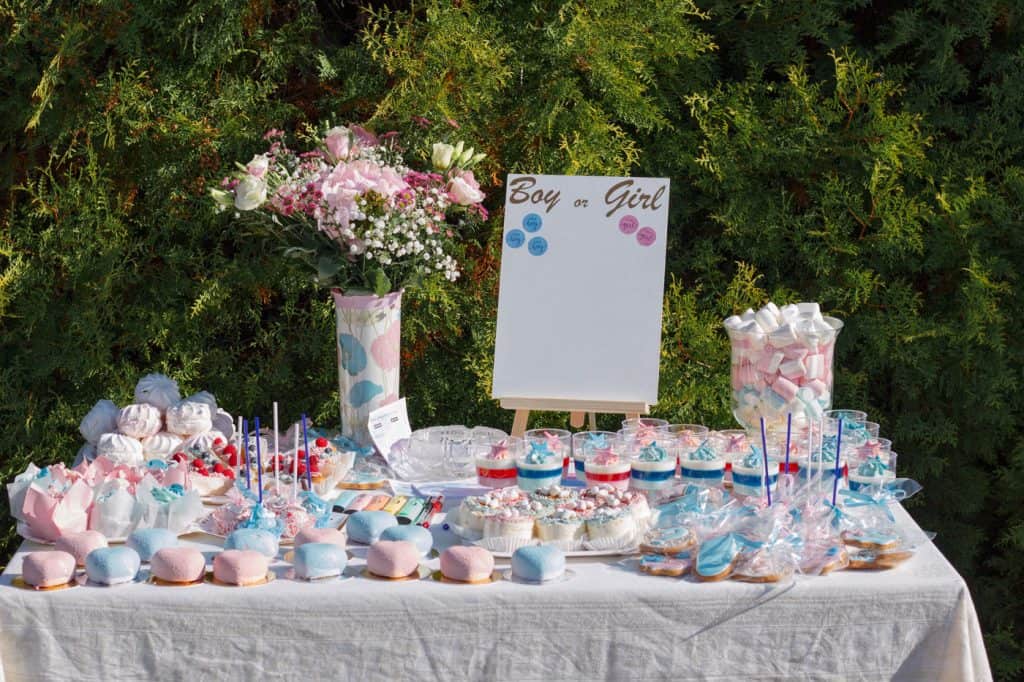 Geschenkideen für babypartys – geschenke für babys, tipps für eltern, schwangere 6 Geschlechtsenthüllungsfeier-Tisch mit rosa und blauen Kuchen, Blumen und Dekoration.