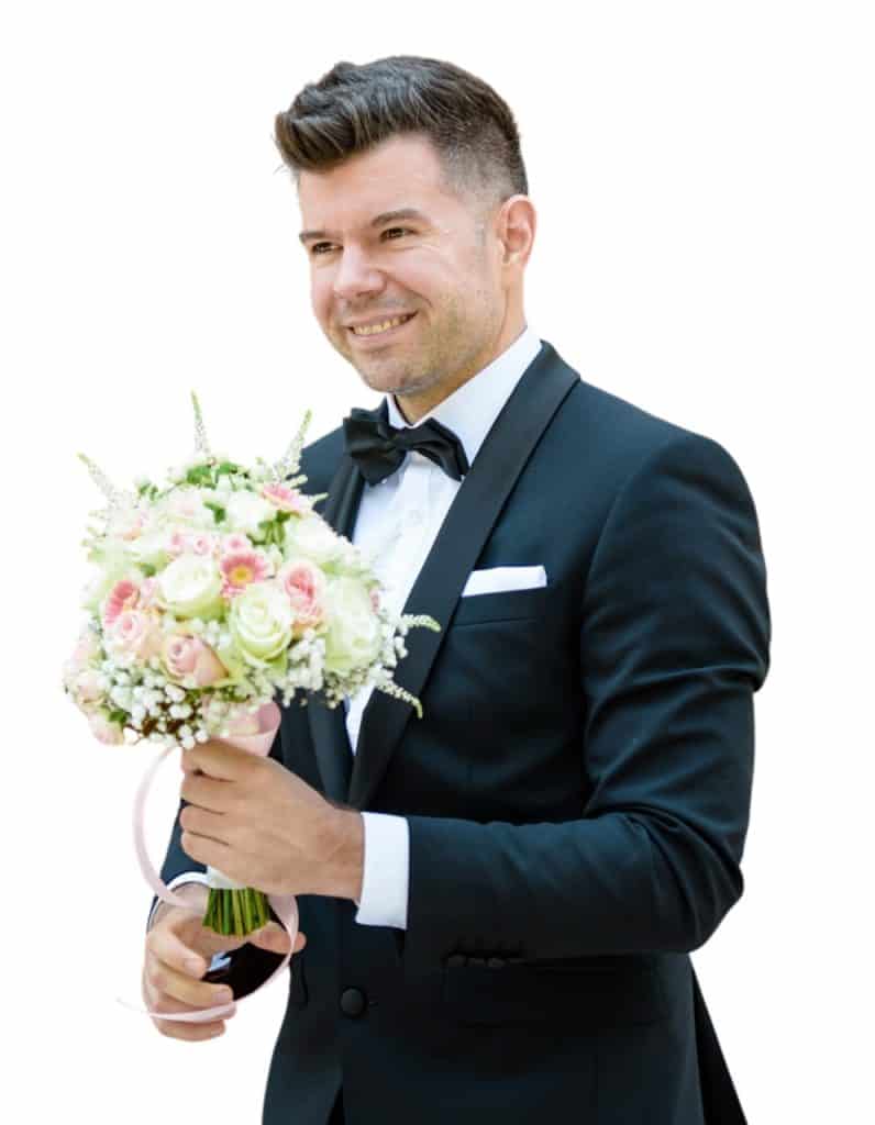 Top8 master of ceremonies in 2026 / the best masters of ceremonies for your wedding 5 Man in suit with black bow tie, holding a colorful bouquet of flowers in his hand.