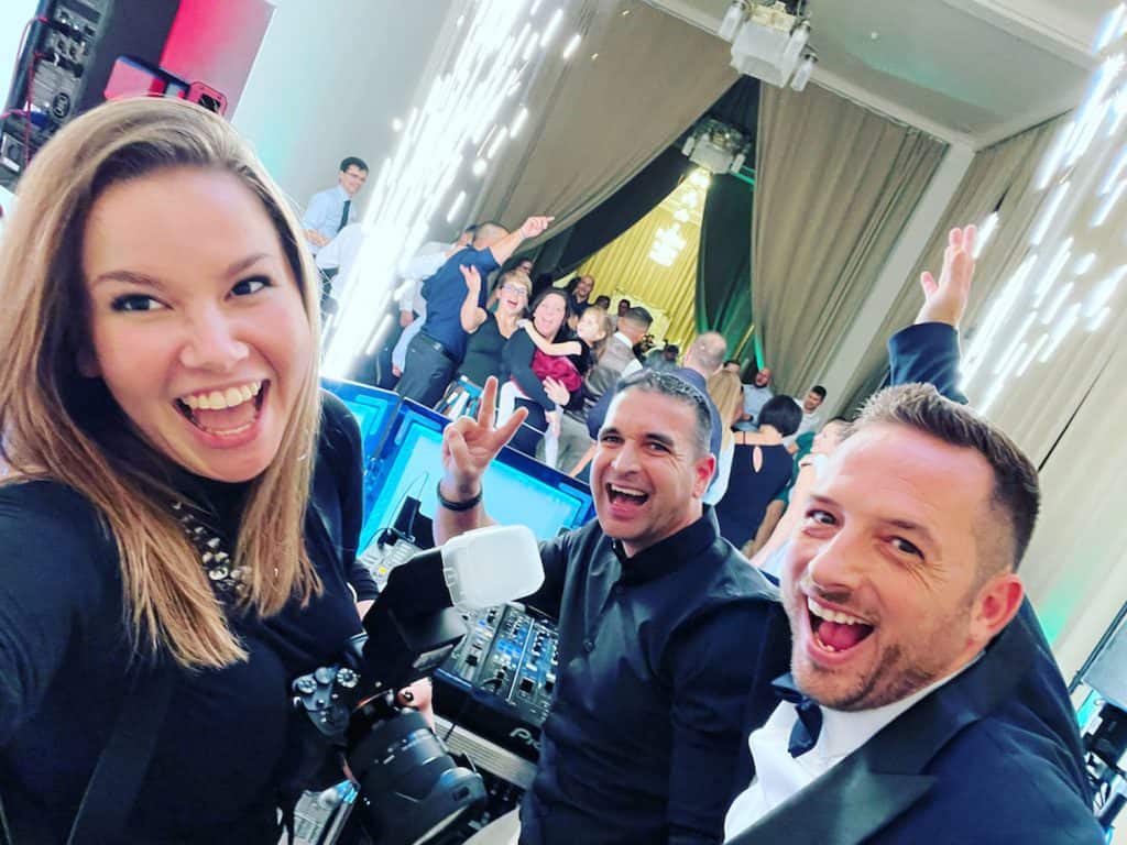 Top8 master of ceremonies in 2026 / the best masters of ceremonies for your wedding 19 Three laughing people pose for the camera, with dancing and sprinkle effects in the background.