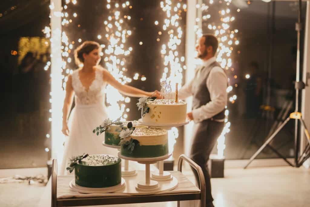 Esküvői pár táncol háromemeletes torta előtt szikrázó háttérrel.