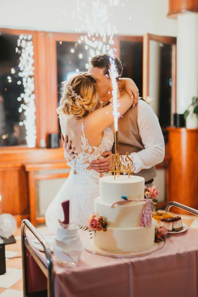 Esküvői pár ölelkezik egy torta előtt, melyen szikrázó tűzijáték és "Mr & Mrs" felirat.