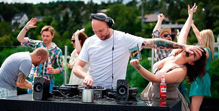 DJ zenét játszik egy szabadtéri eseményen, több ember táncol a háttérben.