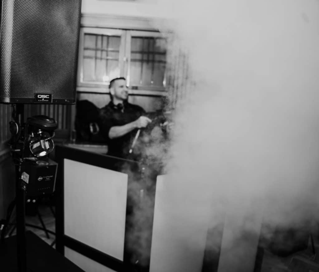 DJ pult és füstgép a zenés eseményen, hangtechnika látható.